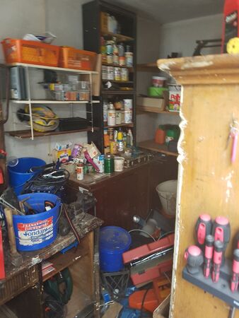 Unordentliche Werkstatt mit Werkzeugen, Regalen, Farbeimern und Schraubenziehern.