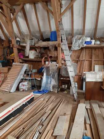 Dachboden mit Holzlatten, Leiter, Baumaterial und gelagerten Werkzeugen im Rohbau.