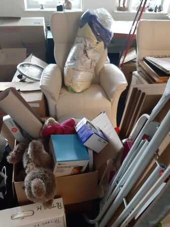 Weiße Ledersessel und Umzugskartons mit Haushaltsgegenständen in einem vollen Raum.